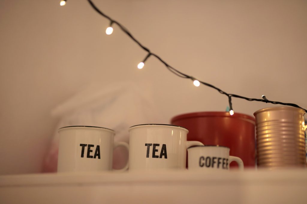 pexels-photo-3916765-3916765 Warm indoor scene with mugs labeled 'Tea' and 'Coffee' under string lights.