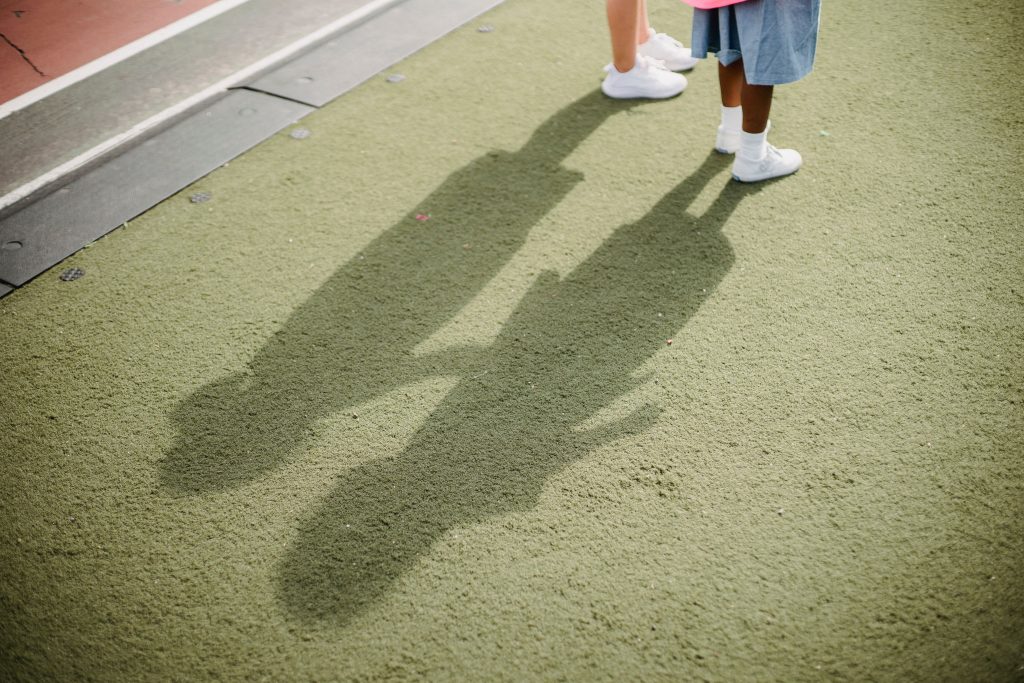 pexels-photo-5275780-5275780 Two children casting shadows on a green school playground surface.